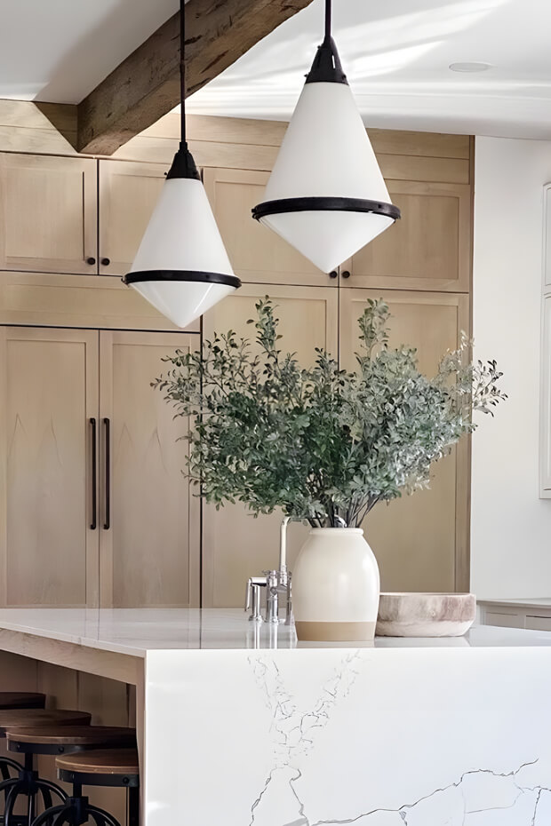 Three-arm pendant lights with white shades hanging from wooden beam above kitchen island